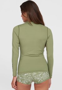 Olivgrünes langärmliges Rashguard mit Flatlock-Nähten und Logodetail. Kombiniert mit gemusterten grünen Shorts mit einem Blättermuster.