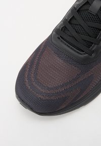 Black athletic shoe with a textured knit upper featuring brown pattern accents, a smooth black rubber sole, and black lace closure.