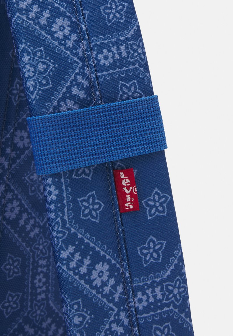 Tissu bleu à motifs avec des designs floraux et géométriques, présentant une sangle en tissu bleu et une étiquette rouge Levi's sur le côté.
