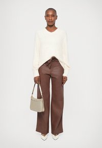 Maglione lavorato a maglia di colore crema con maniche lunghe, abbinato a pantaloni marroni a gamba larga e una piccola borsa grigia chiara. Tacchi bianchi appuntiti completano l'outfit.