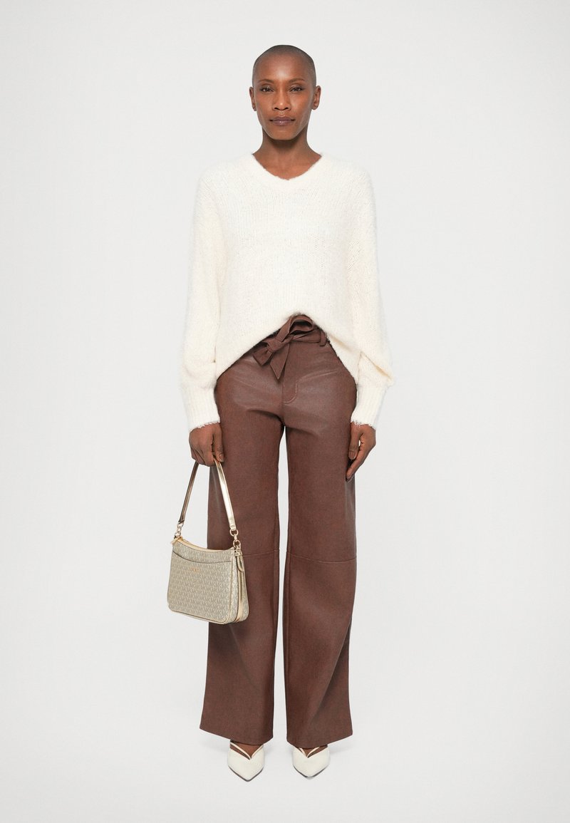 Maglione lavorato a maglia di colore crema con maniche lunghe, abbinato a pantaloni marroni a gamba larga e una piccola borsa grigia chiara. Tacchi bianchi appuntiti completano l'outfit.