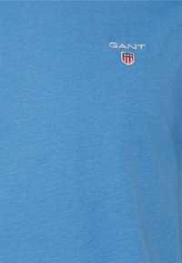 Short-sleeve blue T-shirt made from cotton, featuring a white "GANT" logo and a small shield emblem on the left chest area.