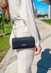 Black quilted handbag with a gold logo, featuring a chain strap and a rectangular shape. The exterior has a textured pattern.