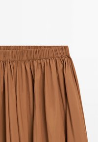 Jupe marron avec tissu froncé et taille élastique visible sur fond blanc.