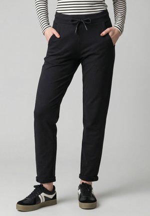 Person wearing black jogger pants with drawstring waist, rolled cuffs, black and white sneakers, and a black-and-white striped long sleeve top.