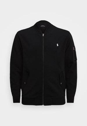 Zwarte bomberjas met ritssluiting, geribde kraag, manchetten, twee voorzakken met klep, ritssluitingzak op de mouw en wit Polo Ralph Lauren-logo op de borst.