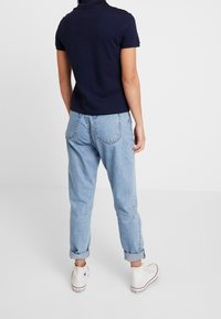 Polo shirt marine à manches courtes associé à un jean en denim bleu clair avec les manches retroussées et des baskets montantes blanches. Tenue simple et décontractée.