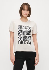 Béžové tričko s krátkým rukávem a leopardím potiskem, které obsahuje černobílé čtverce. Text "DREAM BIG" tučným černým písmem ve spodní části.