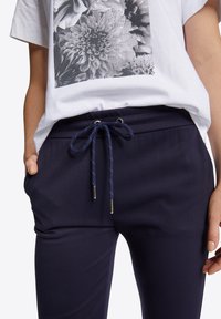 Vit T-shirt med en svart blommig grafik och rund halsringning, matchad med marinblå byxor med dragsko och sidofickor.