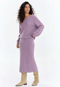 Fioletowy sweter i dopasowany długi sweterkowy komplet, charakteryzujący się przytulną fakturą i luźnym krojem, uzupełniony beżowymi kozakami za kolano.
