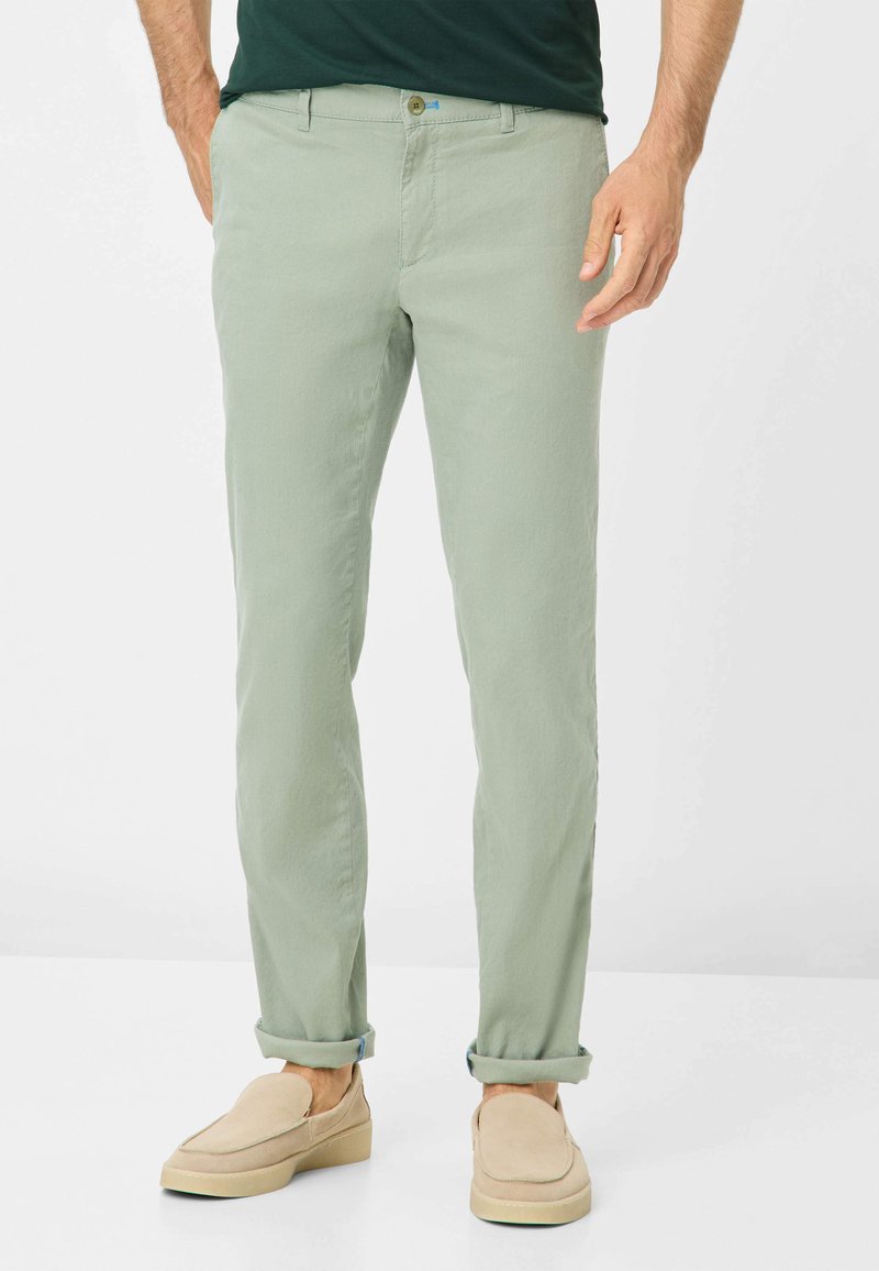 Chino in cotone leggero verde chiaro, con taglio dritto, dotato di chiusura a pulsante e risvolti, abbinati a scarpe beige senza lacci.