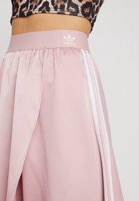 Rosa Adidas kjol med satinfinish, med vita sidostreck och ett brett elastiskt midjeband med Adidas-logotypen.