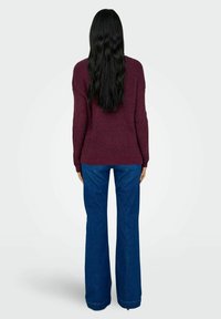Maglione borgogna lavorato a maglia con maniche lunghe, abbinato a jeans in denim blu a gamba larga e alta vita. La texture è rigata e il colore è ricco.
