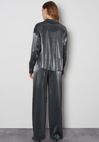 Completo a due pezzi in tessuto grigio scuro lucido. La parte superiore presenta una schiena con colletto, mentre i pantaloni hanno una gamba ampia con una texture liscia.
