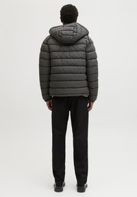 Czarna szara kurtka puchowa z kapturem, z pikowanymi sekcjami, elastycznym dołem, noszona na czarnych spodniach i butach.