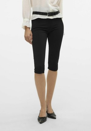 Pantalons capri noirs, ajustés, avec une texture lisse et un ourlet à la cheville, associés à un haut blanc léger et une ceinture noire.