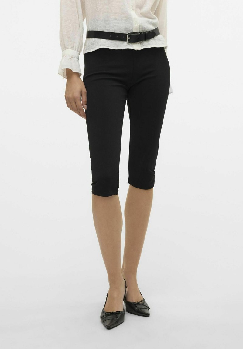 Pantalons capri noirs, ajustés, avec une texture lisse et un ourlet à la cheville, associés à un haut blanc léger et une ceinture noire.