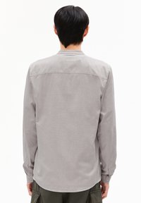 Lichtgrijs langemouwen shirt van een gladde stof. Heeft een button-down kraag en manchetten, met een rechte zoom en een eenvoudig ontwerp.