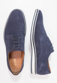 Chaussures en daim bleu marine à profil bas, bout rond et design à lacets. Semelle en caoutchouc blanche avec accents noirs et semelle intérieure en cuir marron.