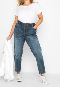 Blå denimjeans med elastisk midjeband, med en framknäppning och två sidofickor. Kombinerade med en vit t-shirt och sneakers.