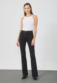 Jeans de campana negros de cintura alta combinados con una camiseta sin mangas de canalé blanca. Los jeans cuentan con dos bolsillos traseros y un cierre con botón en la cintura.