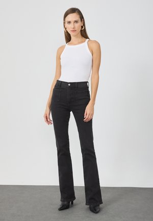 Black high-waisted flared jeans paired with a white ribbed tank top. The jeans feature two back pockets and a buttoned waist.