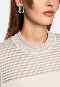 Hellgraues Top mit horizontalen Streifen und einem gerippten runden Halsausschnitt. Große silberne quadratische Ohrringe ergänzen das Design. Glatte Textur.