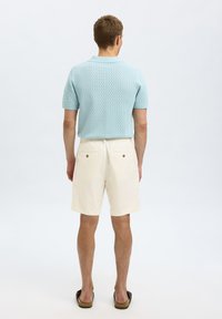 Polo en tricot bleu clair avec un motif texturé, associé à un short couleur crème avec des poches arrière et des accents de bouton.