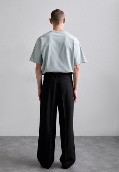 T-shirt bleu clair à manches courtes avec une coupe décontractée associé à un pantalon large noir taille haute, vu de dos.