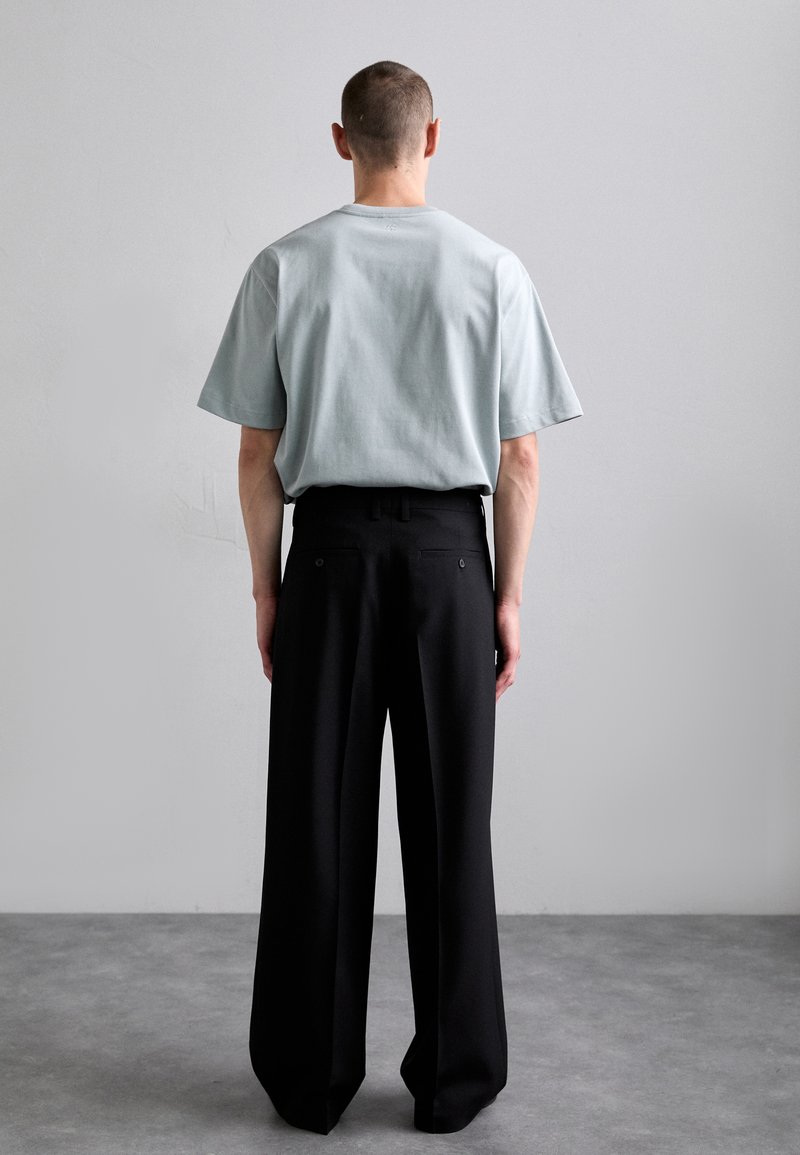 Light blue short-sleeve t-shirt with a relaxed fit paired with high-waisted black wide-leg trousers, viewed from the back.