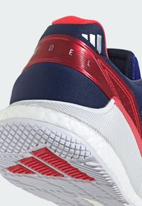 Navy blue athletic shoe with red accents. Features a textured sole, smooth heel cap, and cushioned white midsole with patterned grip.