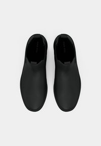 Sorte slip-on sko med en glat mat finish, rundet design og trækflapper for nem påtagning. Har en polstret indvendig del for komfort.