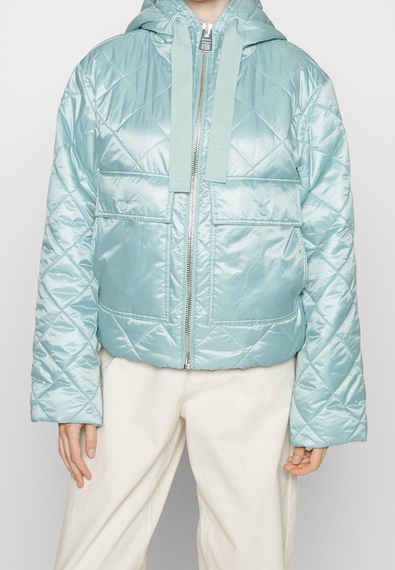 Helle blaue gesteppte Pufferjacke mit Kapuze, ausgestattet mit einem Frontreißverschluss, zwei großen Taschen und strukturierter Oberfläche.