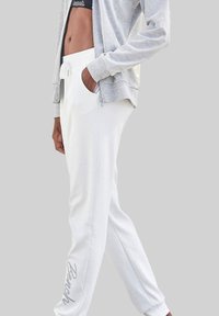 White sweatpants with drawstring waist, featuring a side pocket and "Bench" embroidered in silver on the left leg. Gray zip-up jacket.
