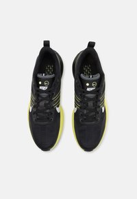 Fekete Nike futócipők, hálós felsőrésszel, lime zöld kiegészítőkkel, fehér swoosh-szal és textúrázott talpdesignnal.