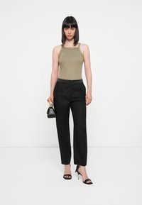 Olivgrön linne, svarta texturerade högmidjade byxor, svarta remsandaler med klack och en liten svart handväska med metalliska detaljer.