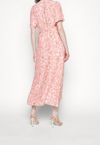 Vestido midi floral en rosa con mangas cortas, que presenta una cintura ajustada y una falda acampanada. Combinado con zapatos de tacón blancos con tiras.