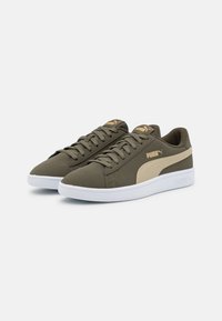 Sneaker verde oliva con suole bianche, dotati di una striscia laterale beige e dettagli in oro. Texture liscia e design classico con lacci.