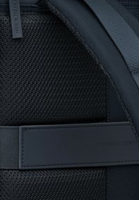Zwarte rugzakinterieur met een mesh-textuur, gladde stof en een leren strap met de geperste tekst "MADE FOR EXPERIENCE."