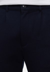 Fekete formális nadrág gombos záródással és övbújtatókkal, elölről, deréktájon látható.