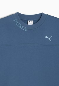 Blå bomulds sweatshirt med rund hals, prydet med broderet Puma-logo og et falmet print af "PUMA" på skulderen. Glat tekstur.