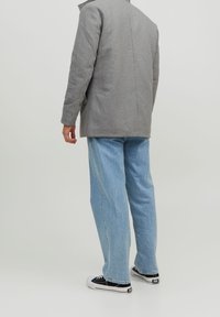 Grå ullkappa med skräddarsytt snitt, kombinerad med lösa ljusblå jeans och svarta canvas sneakers. Mjuk tygstruktur, minimal detaljering.