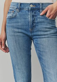 Világoskék, slim fit farmernadrág, öt zsebbel, kontrasztos varrással és fém gombos záródással a deréknál.