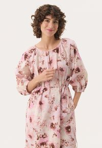 Robe florale mettant en avant des tons roses et marron, tissu texturé, manches bouffantes, col rond et taille cintrée avec un détail à nouer.