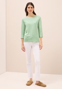 Zielono-białe paskowane długie rękawy w zestawieniu z białymi spodniami i beżowymi butami wsuwanymi, charakteryzujące się luźnym krojem i miękkim materiałem.