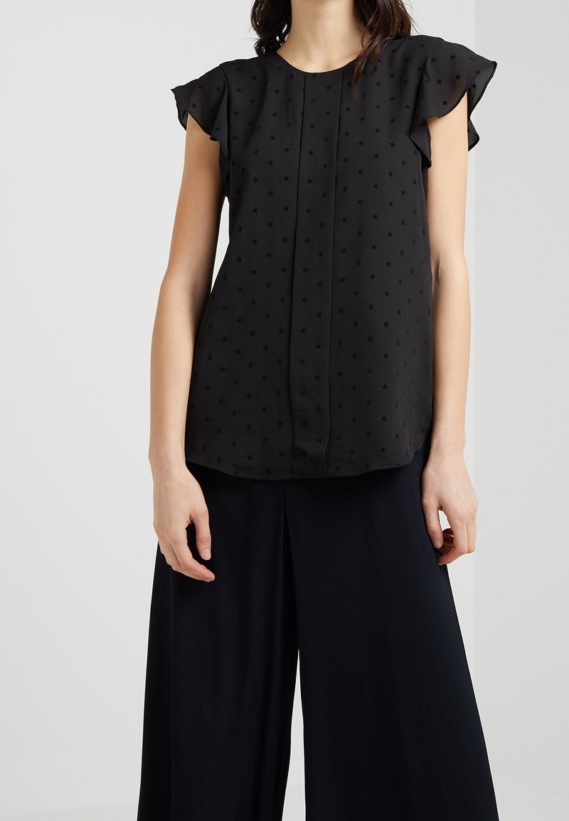 Svart blus med korta, volangärmar och en subtil stjärnpattern. Slät tyg, rund halsringning och rak fåll.