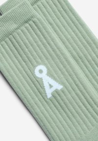 Calzini a costine verde chiaro con un logo bianco. La texture è morbida con un design tradizionale da calzino e una vestibilità aderente nella parte superiore.