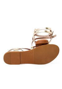 Sandal s popruhmi a hnedou gumovou podrážkou, zlatými kovovými akcentmi a textúrovanou stielkou. Obsahuje dva nastaviteľné popruhy pre lepšie prispôsobenie.