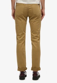 Pantalones de algodón beige con un diseño ajustado, que presentan puños enrollados y dos bolsillos traseros con un acabado texturizado.