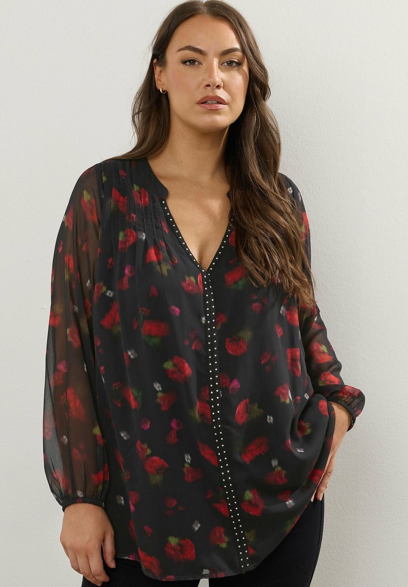Svart genomskinlig blus med röd och grön blommönster. Har en V-ringning, långa puffärmar och silverstudsar längs framkanten.